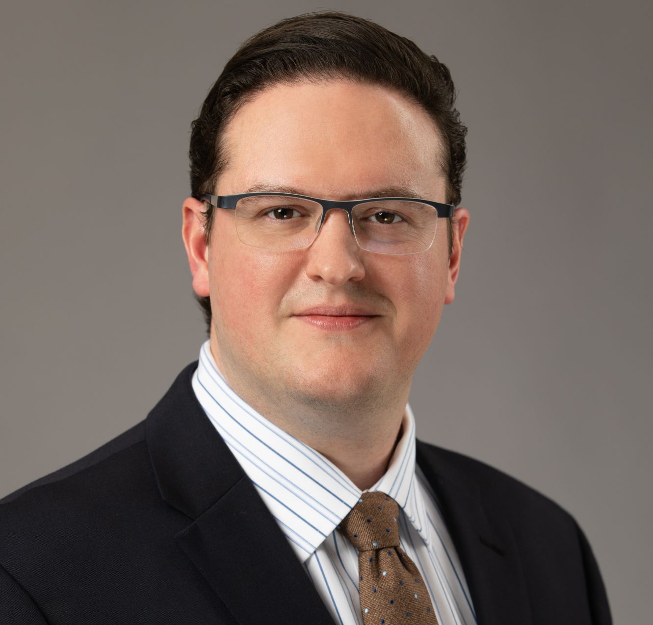 Headshot for small business and startup attorney, Jeffrey R. Pote, in a navy suit and brown tie in front of a gray background