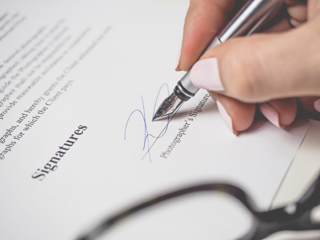 a close-up image of a business woman's hand signing a contract with a silver pen.