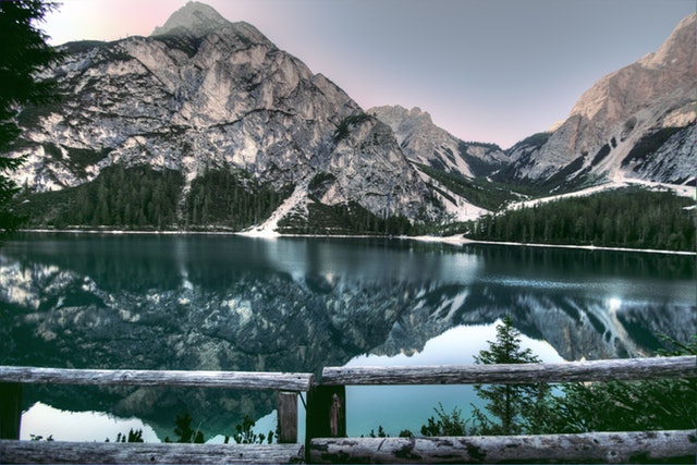Tall granite mountains tower behind a still blue lake in the Rocky Mountains during winter